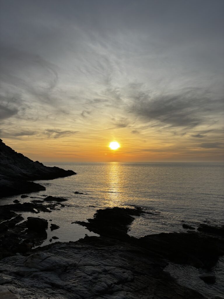 Coucher de soleil sur la mer en Corse au mois de mai, avec côte rocheuse et reflets dorés, illustrant la beauté des paysages corses au printemps.