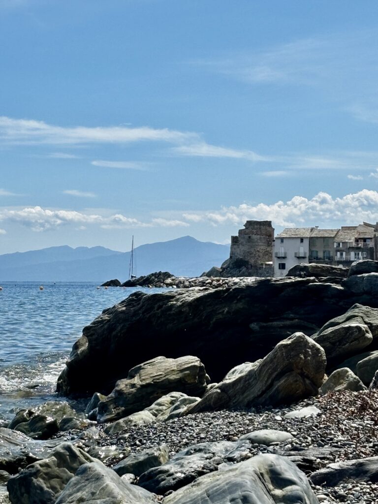 Village corse en bord de mer au printemps, avec rochers et eau turquoise, illustrant le charme authentique de la Corse en mai.